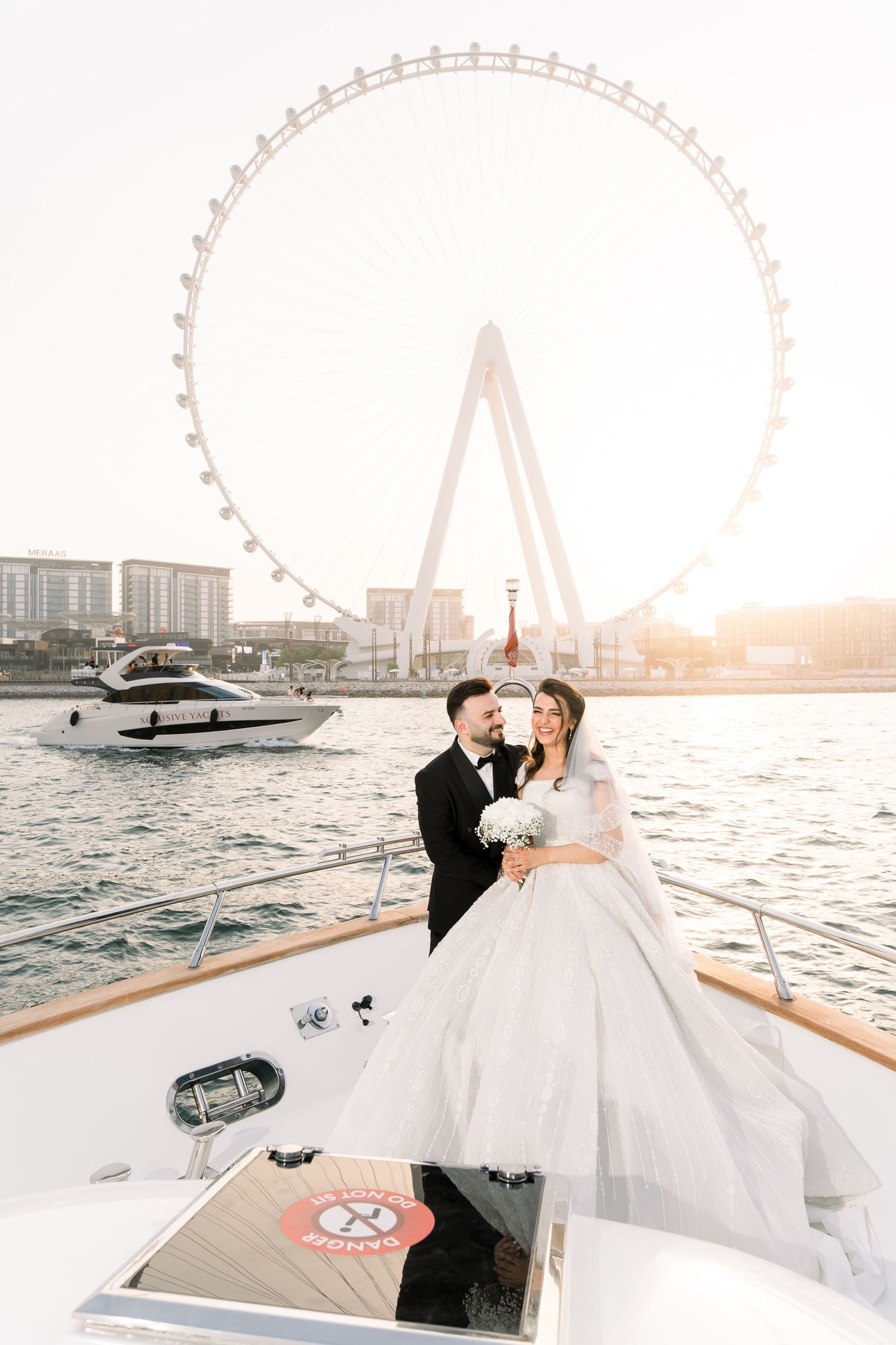 Happy couple celebrating their wedding on a luxury yacht with Dubai Eye Ferris wheel in background at sunset.
