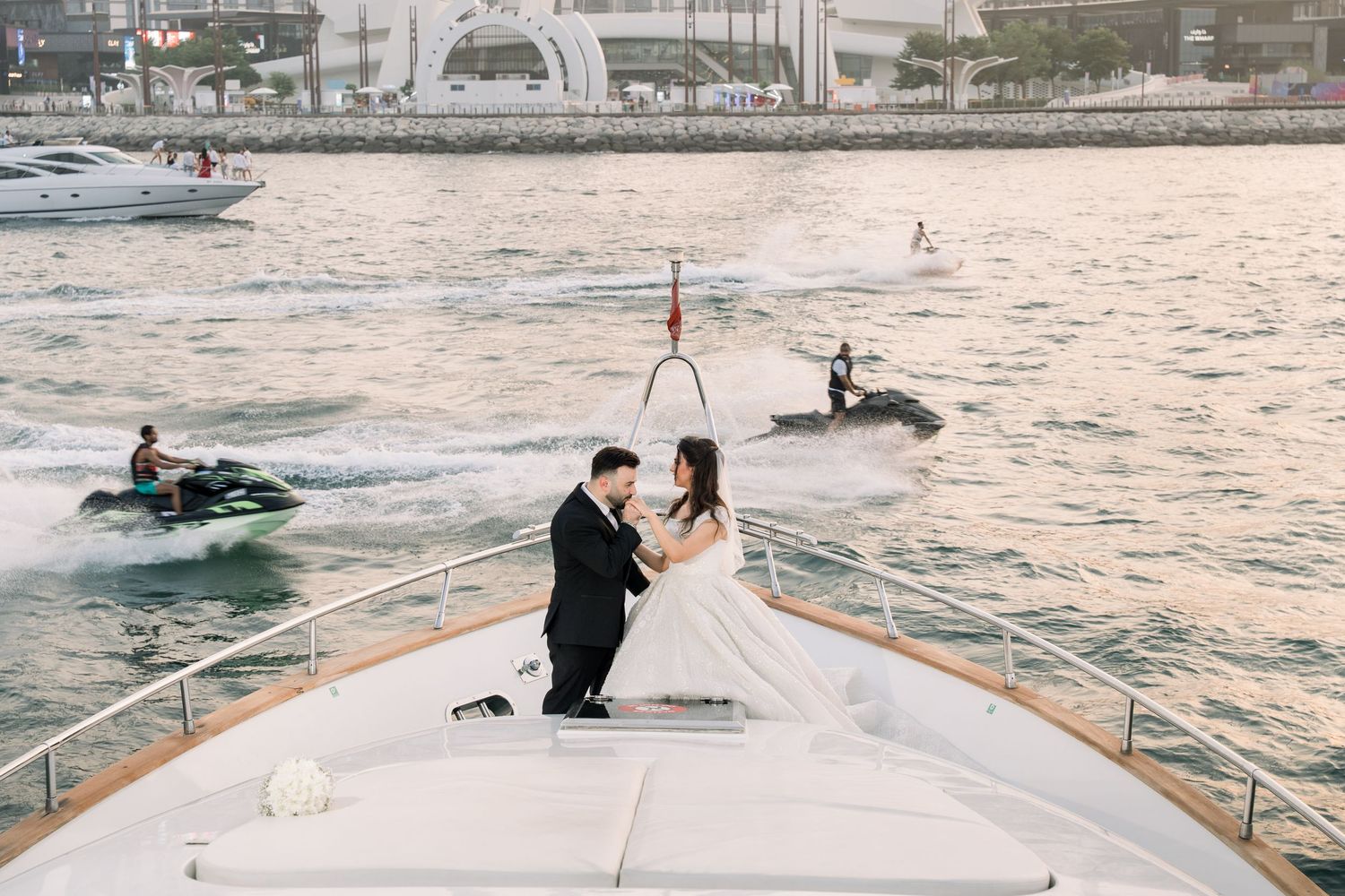 Luxury yacht cruises at sunset with jet skis following in its wake on tranquil waters.