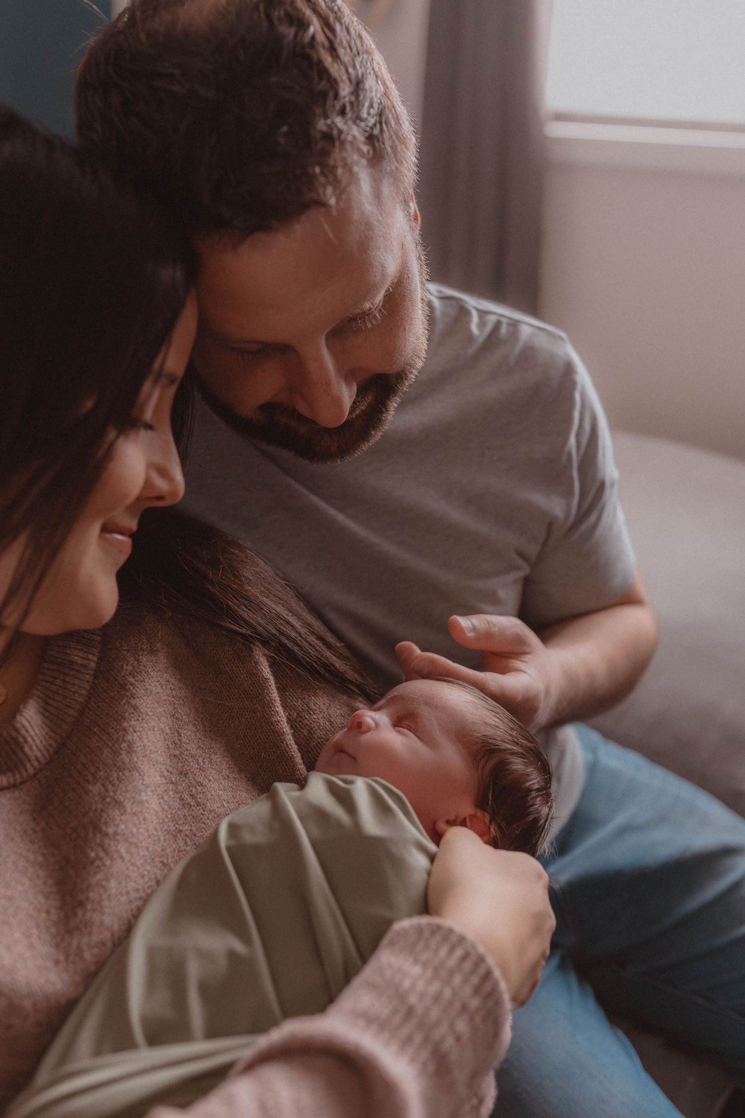 New parents smiling and bonding with their newborn baby in a warm, softly lit home setting.