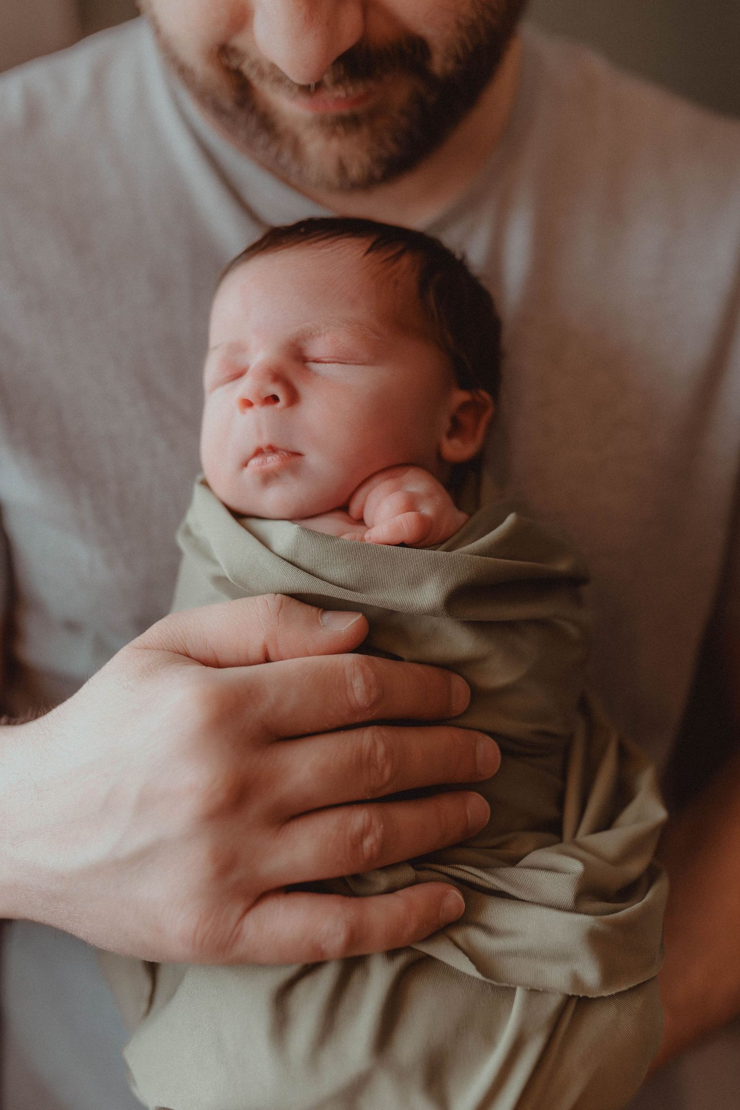 Father holding swaddled newborn baby in his arms during intimate family moment at home.
