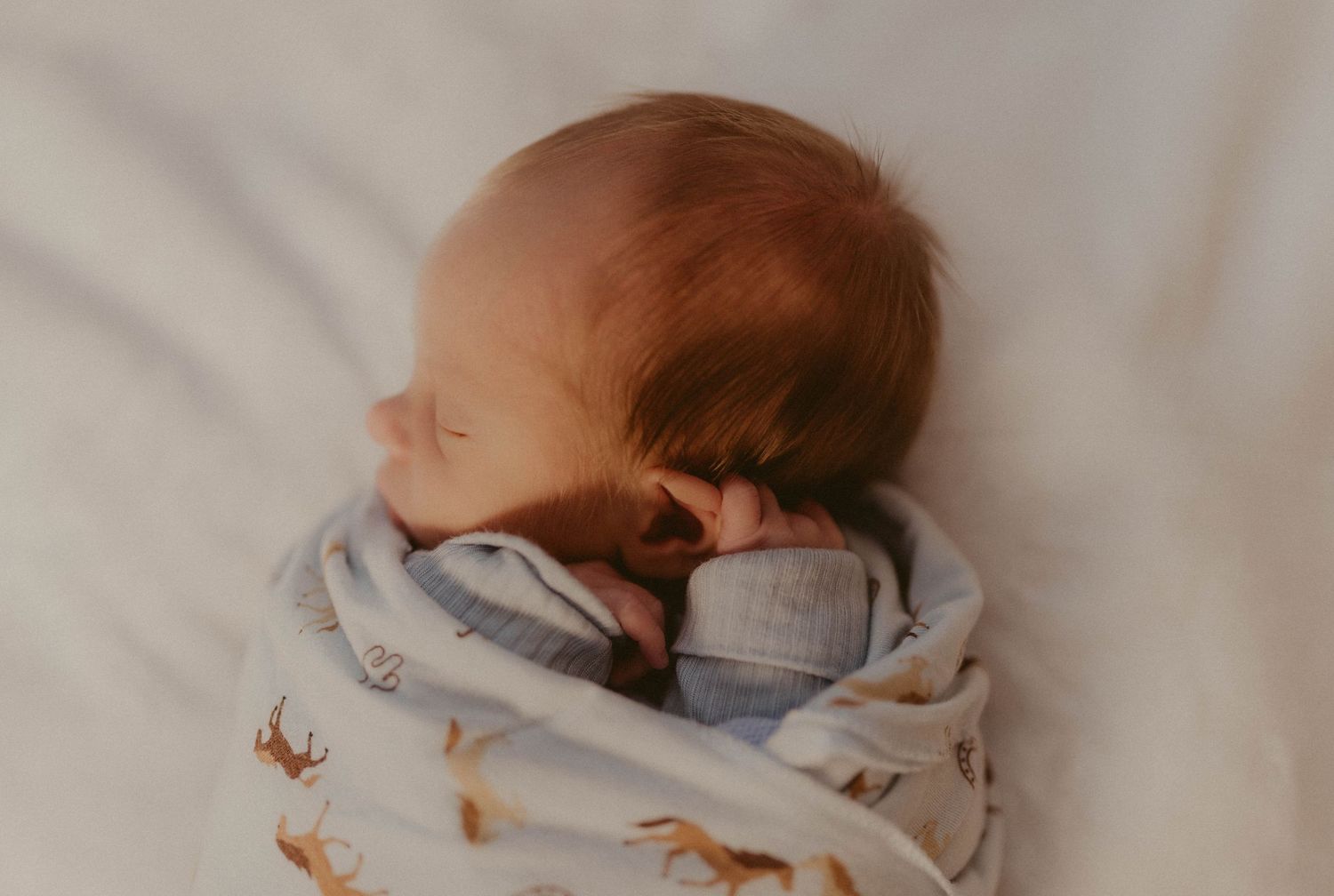 Peaceful newborn baby sleeping swaddled in a soft patterned blanket with tiny hand near face.