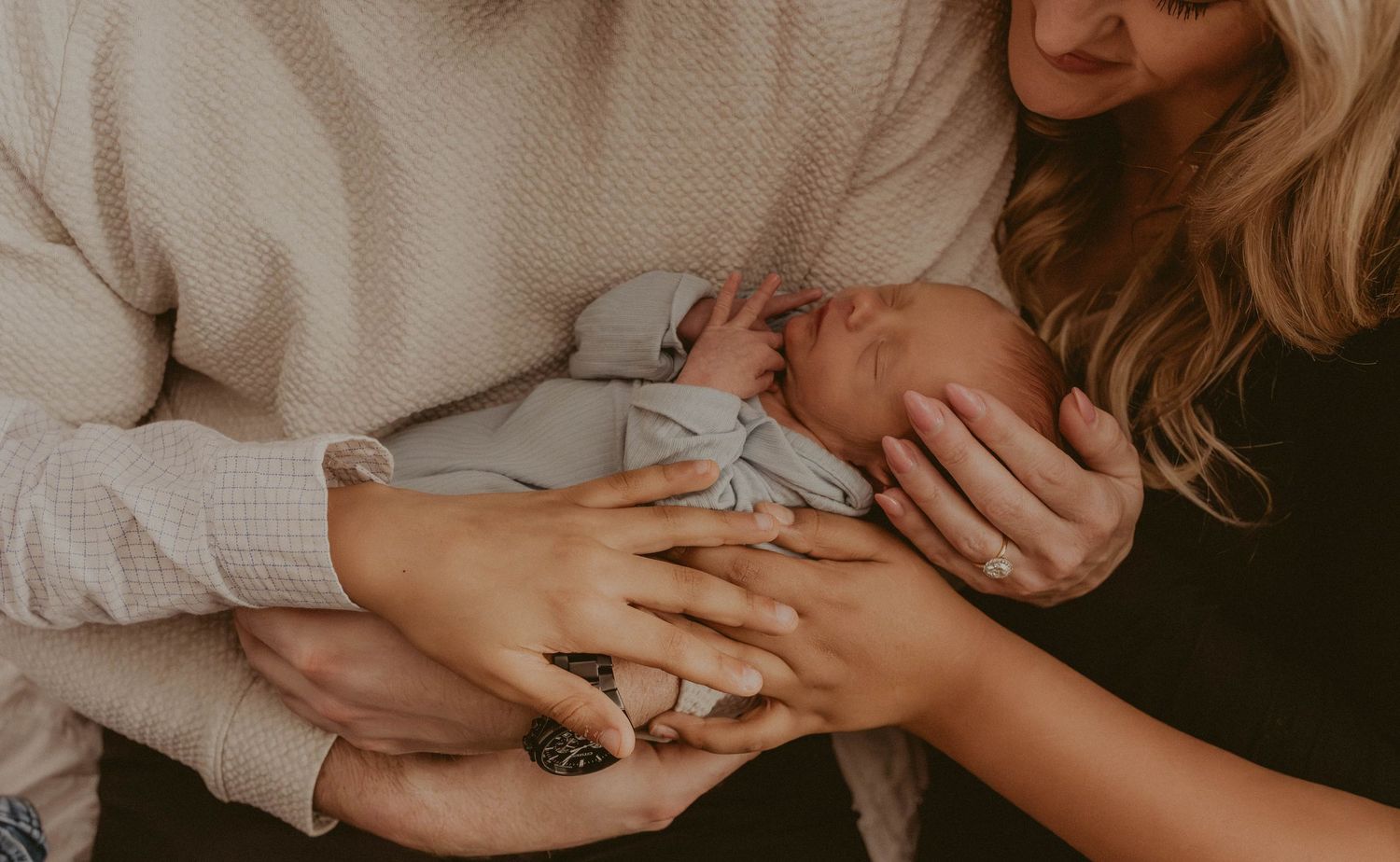 Parents cradling a sleeping newborn baby in their hands, a tender family moment captured in warm, neutral tones.