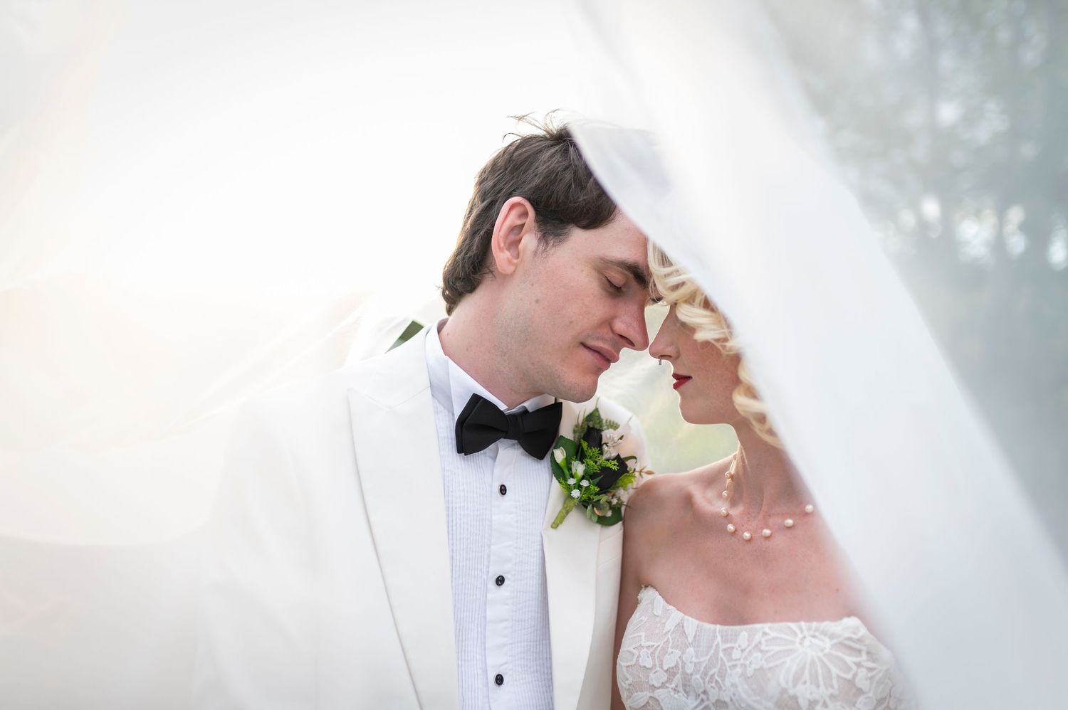 A tender moment shared between newlyweds under soft lighting with white veil and formal wedding attire.