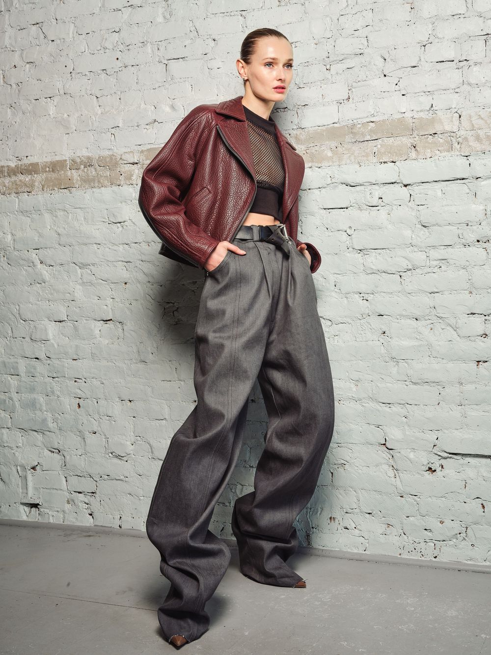 Oversized grey trousers paired with burgundy leather jacket in avant-garde fashion shoot.