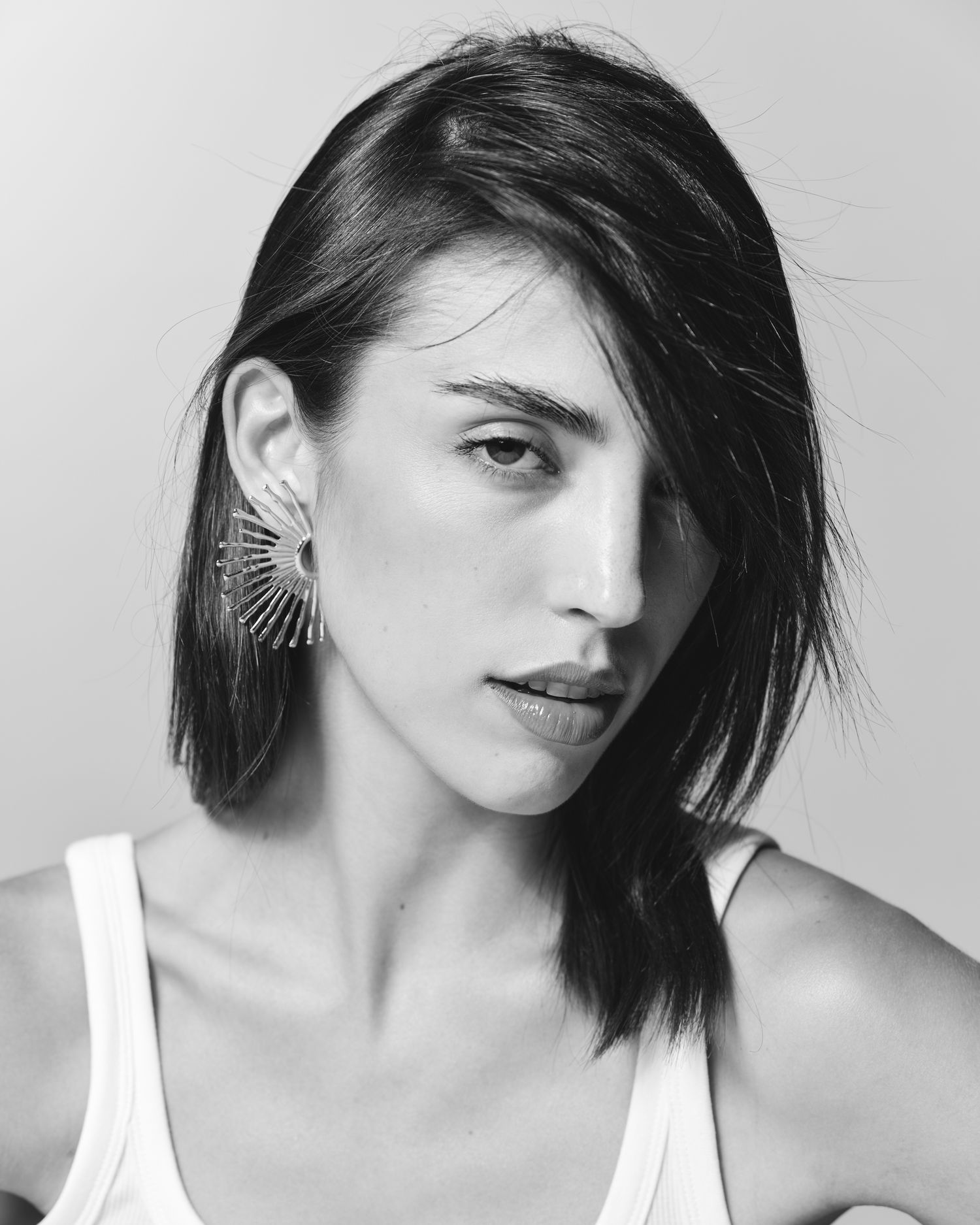 Black and white portrait of a young woman with dark bob hair wearing a sunburst ear cuff and white tank top.