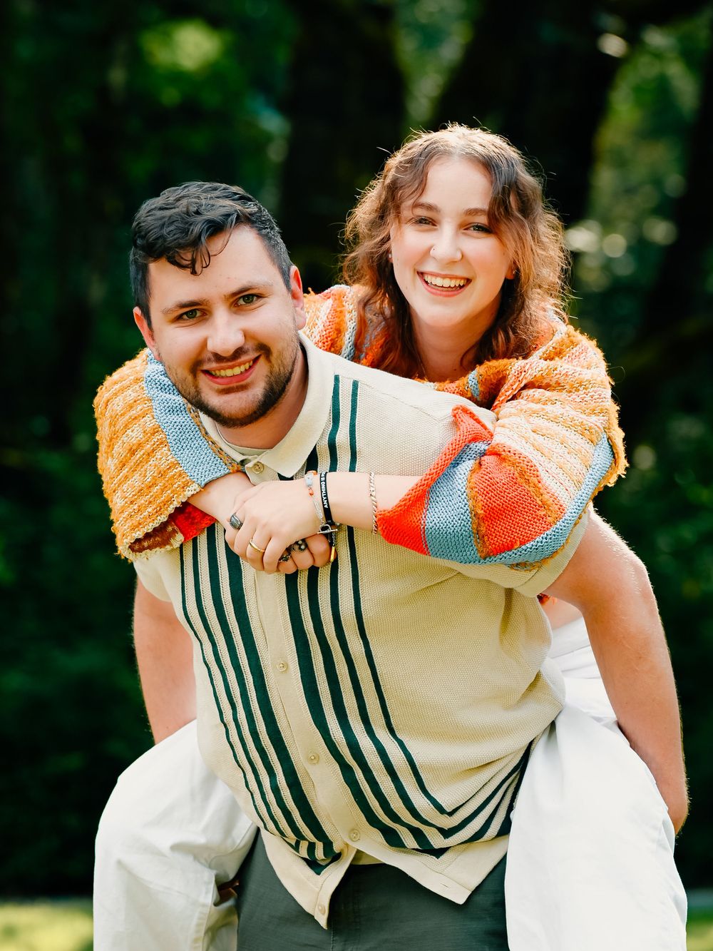 Happy couple plays piggyback in a sunny outdoor setting wearing contrasting orange and striped outfits.