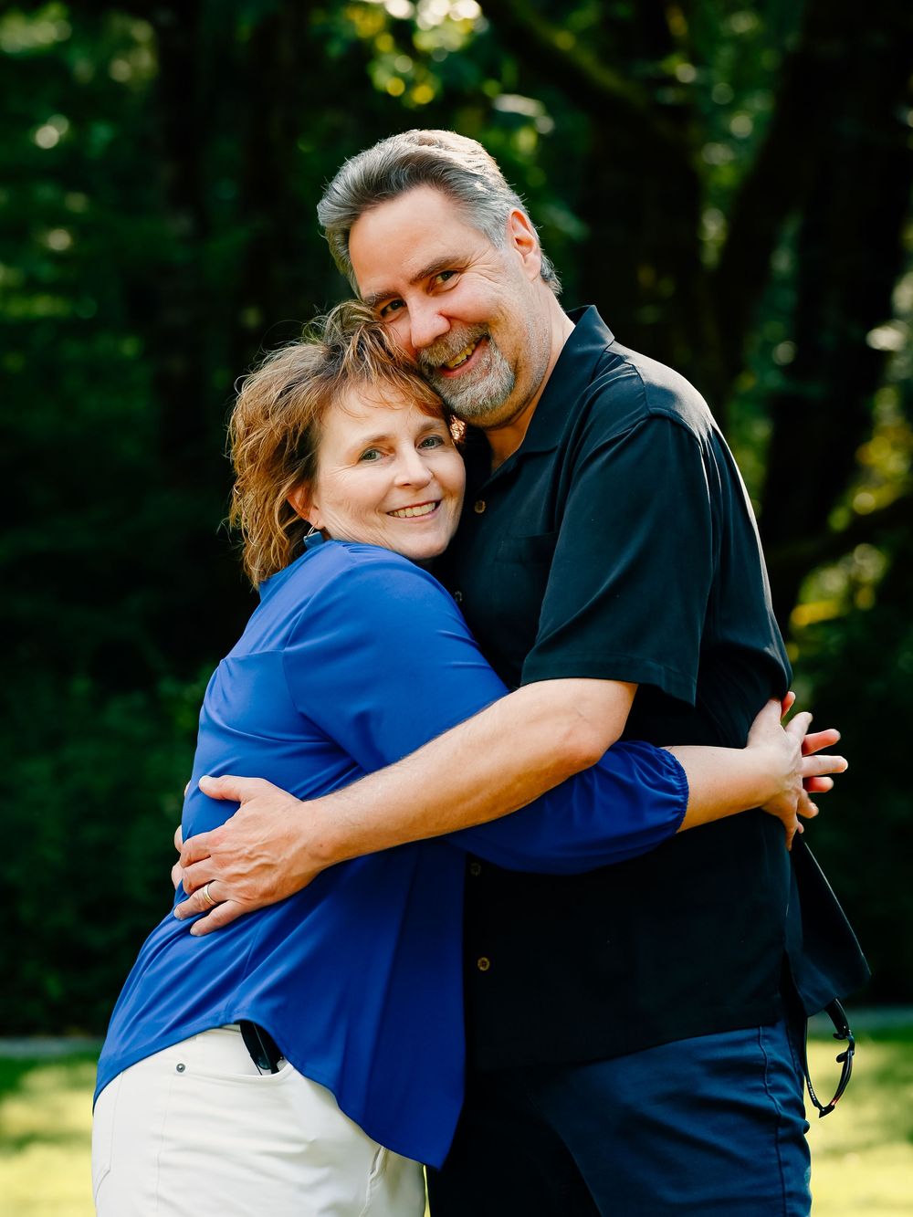 People share warm hugs while posing for casual portraits in a natural outdoor setting.