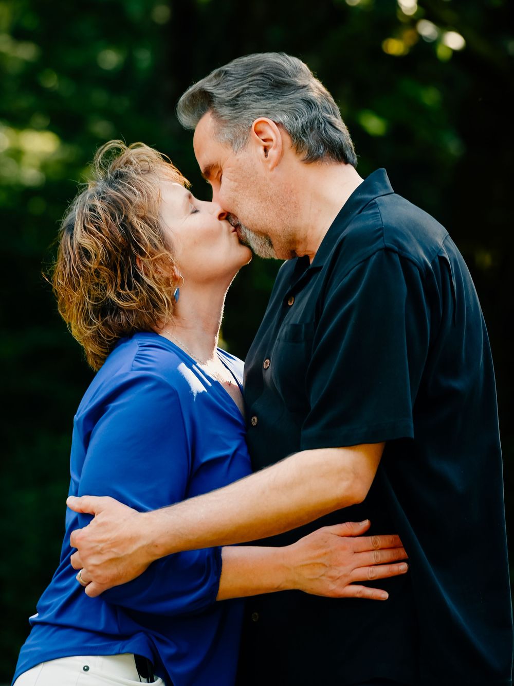 Two people sharing an intimate embrace outdoors against a dark green natural background.