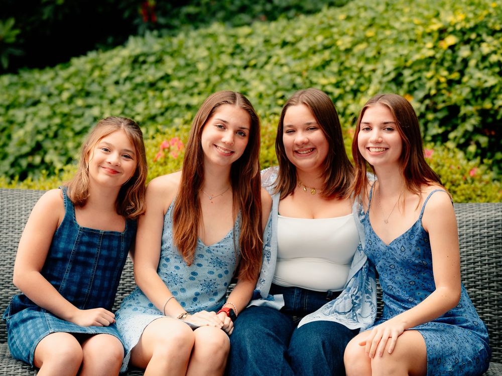 A group wearing blue denim clothing sits together smiling in an outdoor setting with lush greenery in the background.