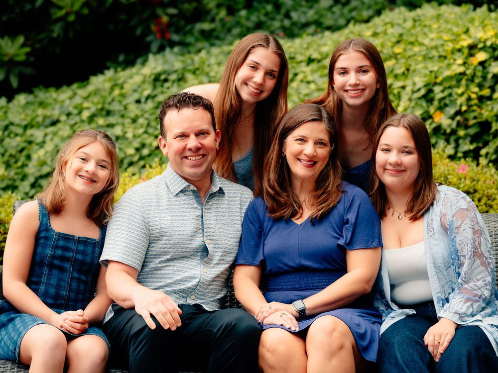 A family sits in a green garden setting wearing coordinated casual outfits in shades of blue and gray.