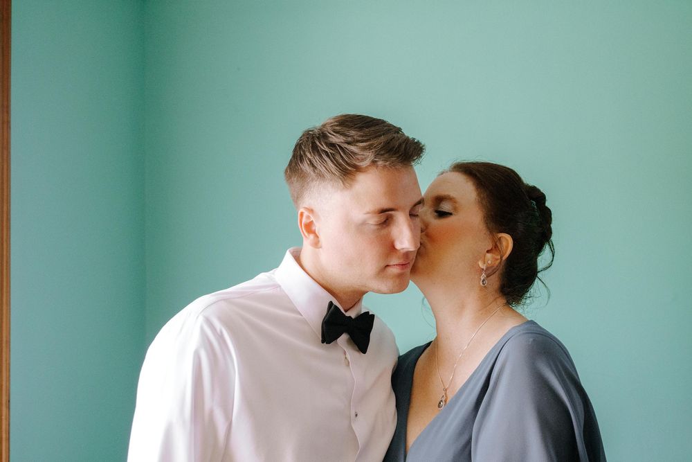An intimate moment shared between a couple against a turquoise wall at a formal event.