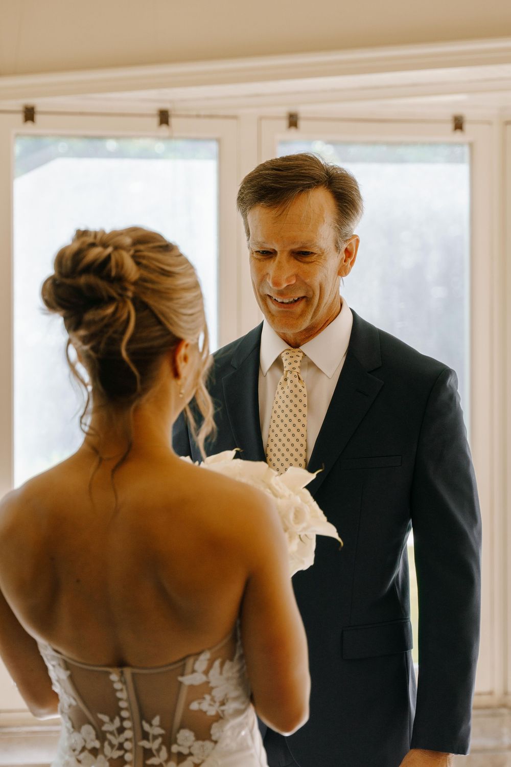 A heartwarming first look moment between a bride in a strapless gown and groom in a dark suit at a sunny venue.