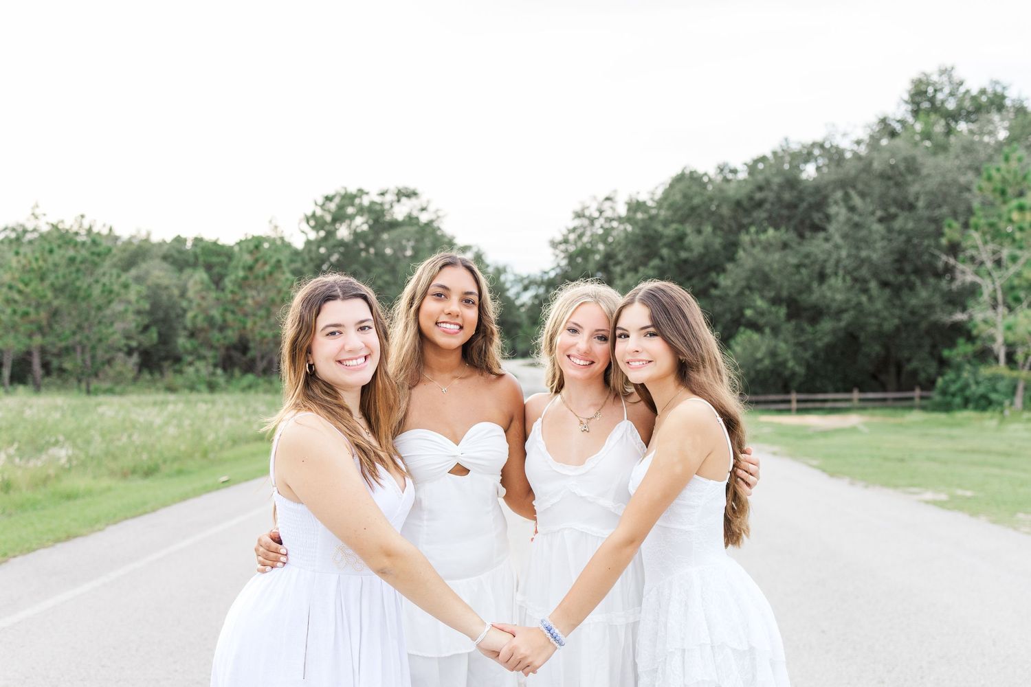 Group photo of friends wearing white dresses standing together outdoors.