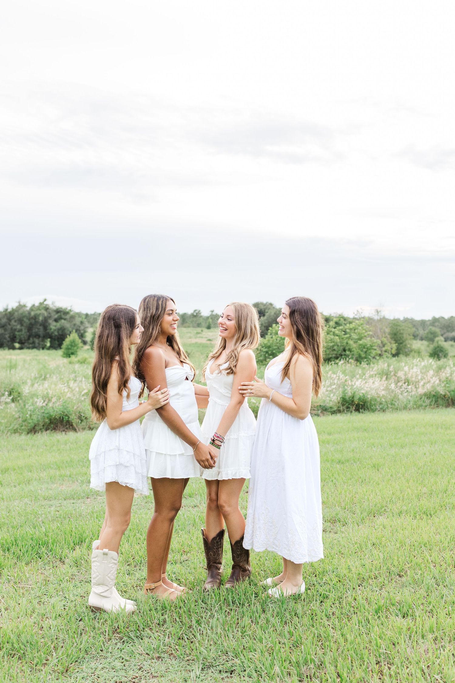 Friends in white dresses laughing together in a sunny field.