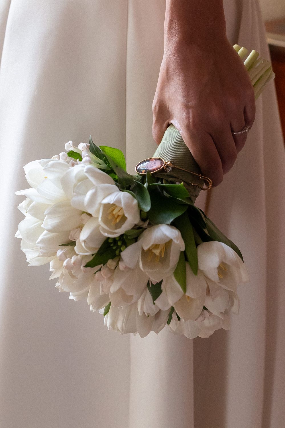 A hand holds an elegant white tulip bouquet against a light cream-colored curtain backdrop.