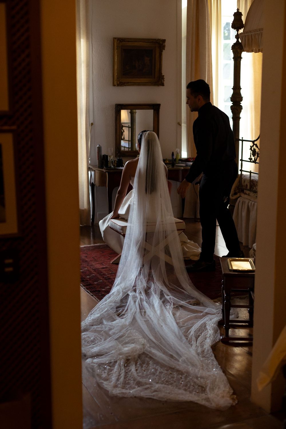 A flowing cathedral-length wedding veil trails elegantly across a hardwood floor in an ornate hallway.