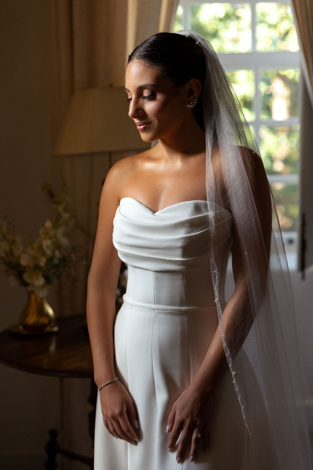 A series of elegant bridal portraits in natural window light showing details of a white wedding gown and flowing veil.