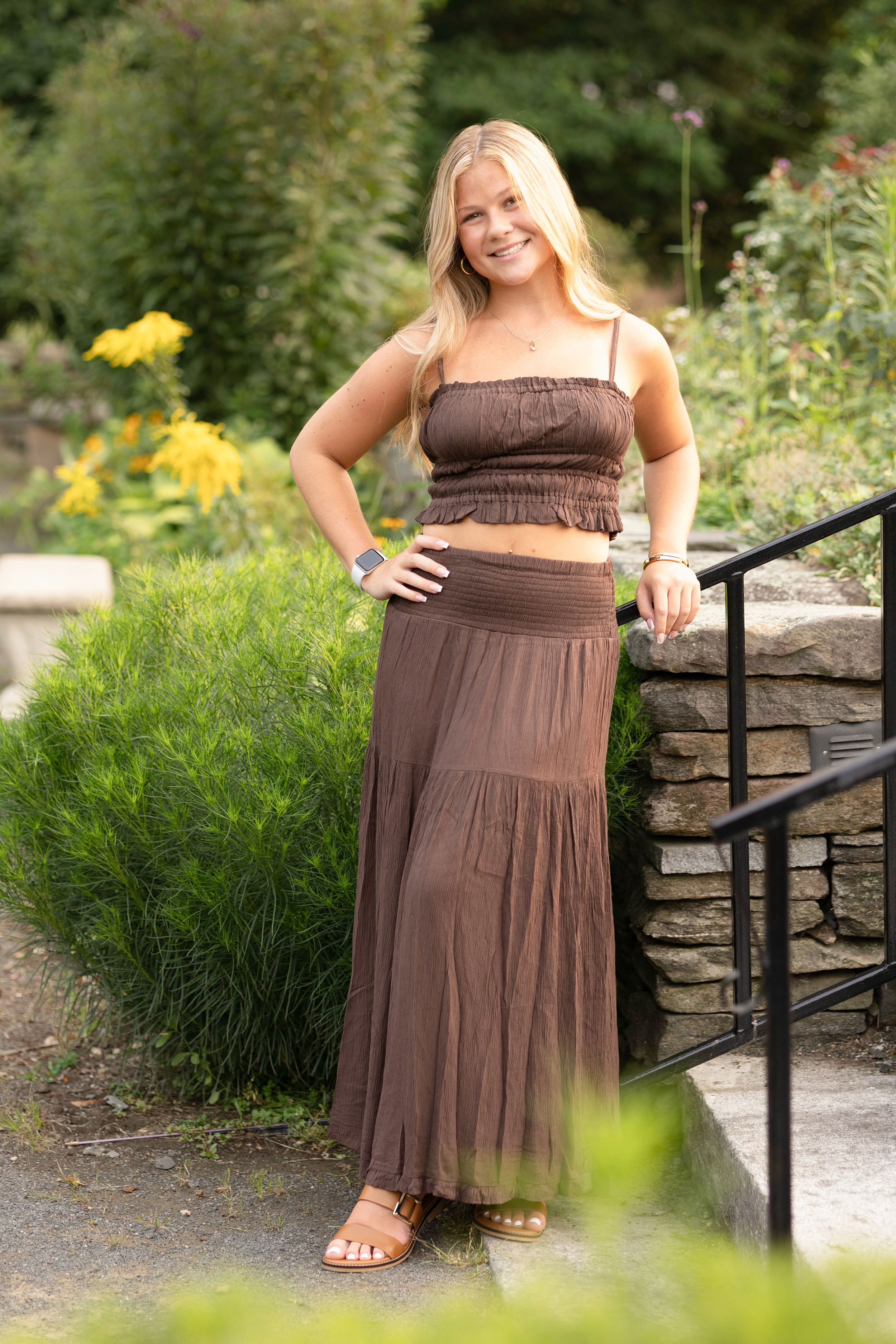 Portrait series in brown dress near stone wall and garden railing.