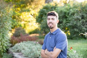 Person in blue polo shirt posing outdoors in natural garden setting during golden hour.