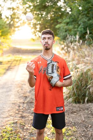 Person wearing orange sports jersey and baseball gloves posing on outdoor path.