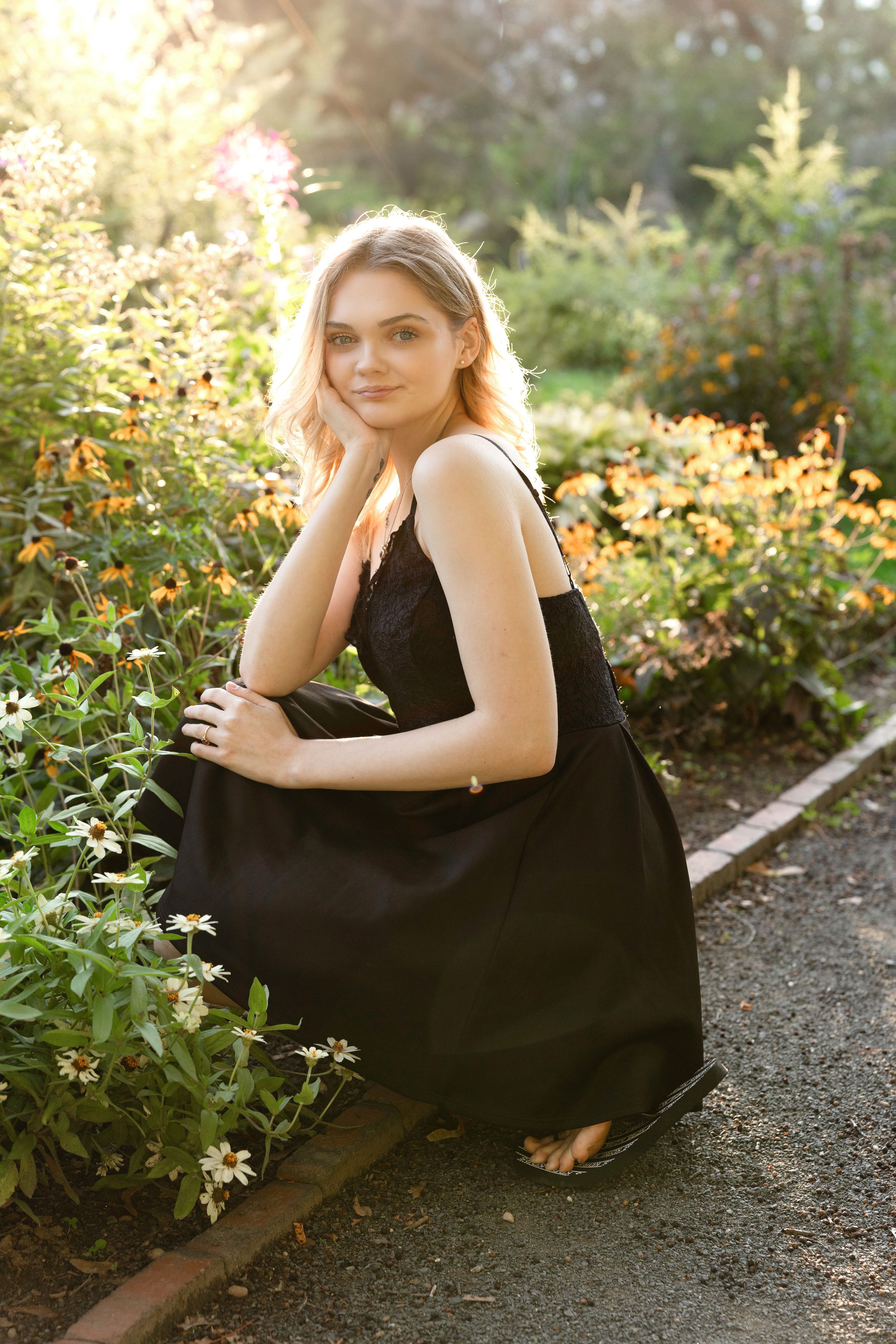 Person in black dress poses on garden path during golden hour sunset.