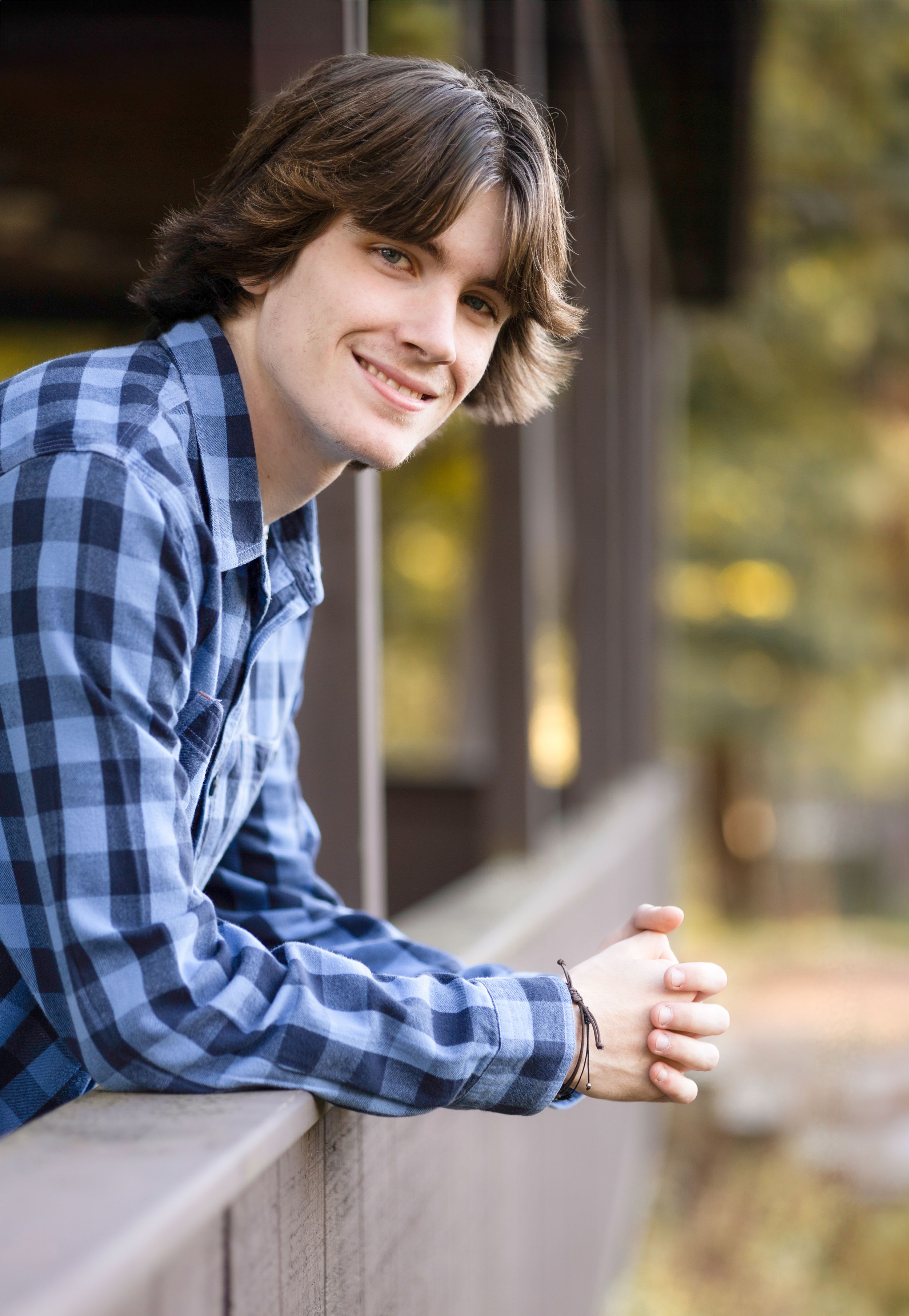 Portrait series in blue plaid shirt leaning on wooden railing.