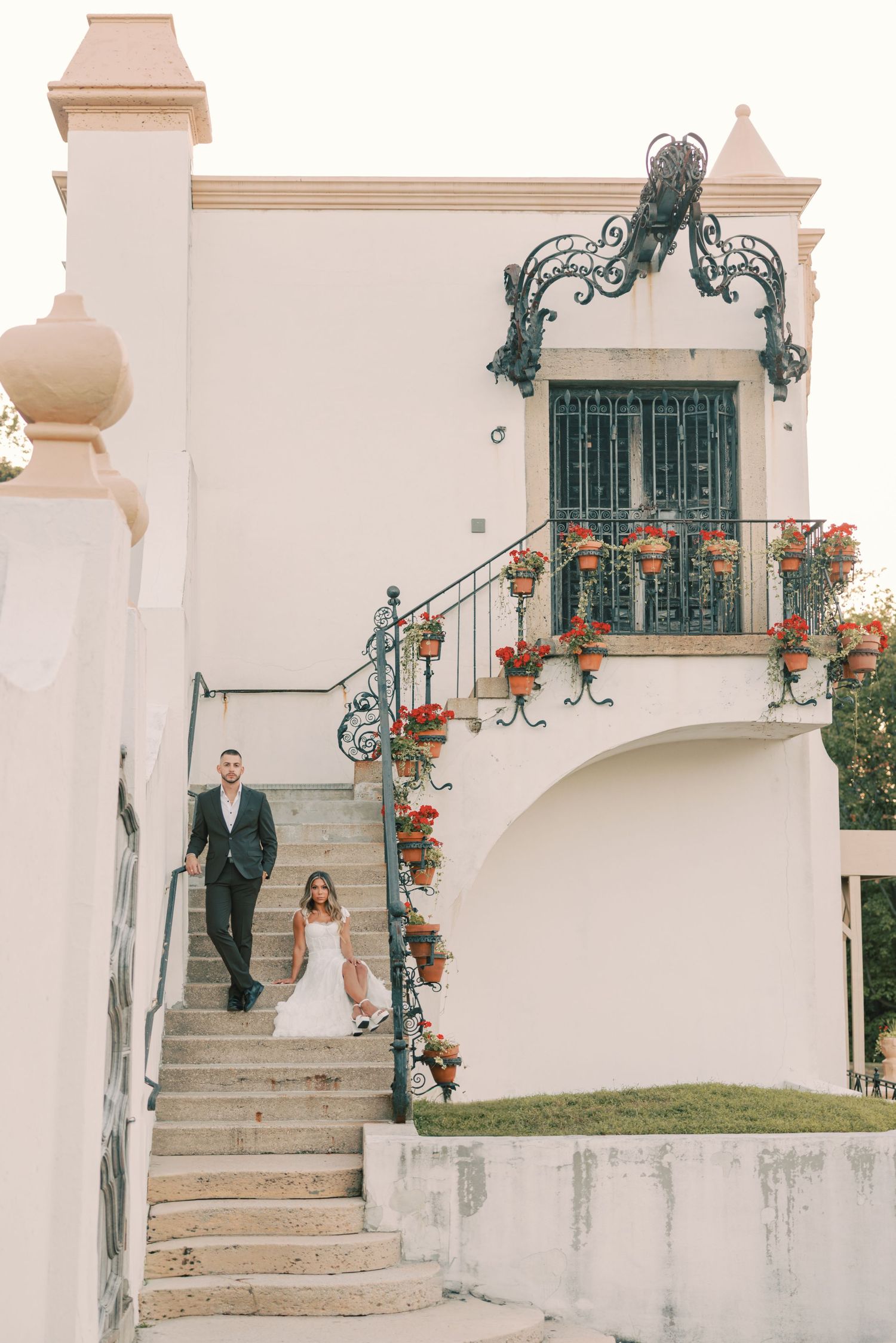 Bride and groom descending ornate wrought iron staircase of white Mediterranean villa at Vanderbilt Museum