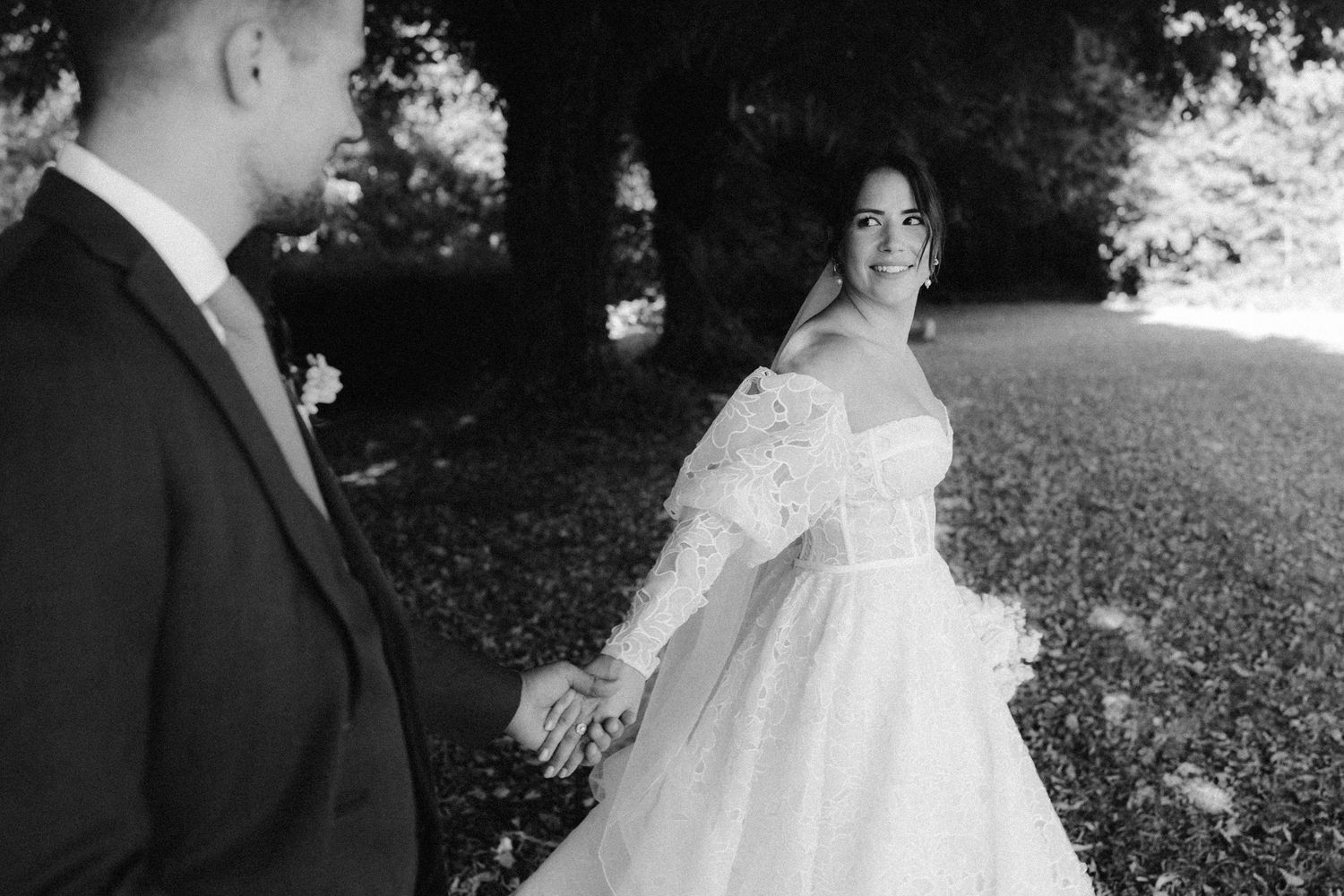 A romantic black and white wedding photograph showing a tender embrace in a natural outdoor setting.