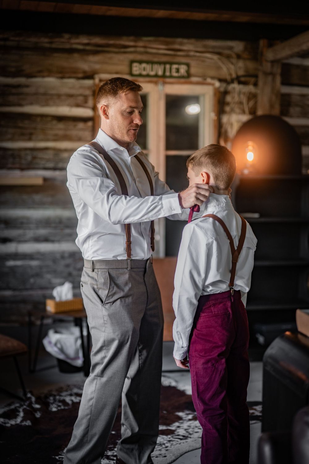 Formal dress preparation scene in rustic cabin with suspenders and bow tie.