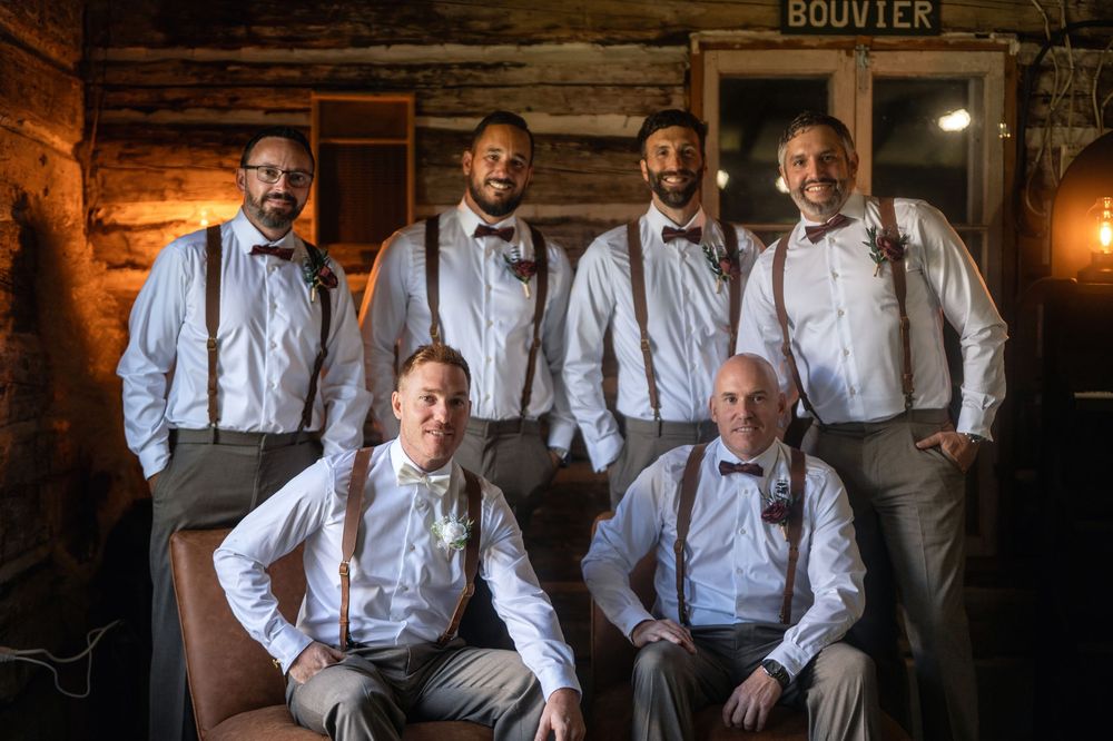 Groomsmen in white shirts and suspenders posing together in rustic wooden venue.
