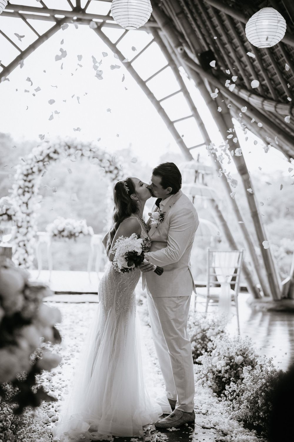 Black and white photo of a romantic moment in a rustic wooden venue with paper lanterns.