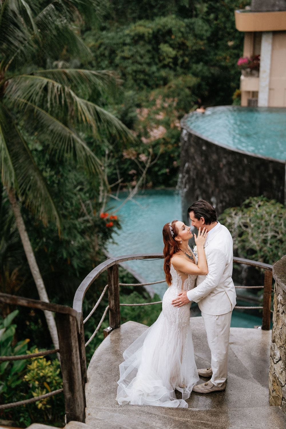 Romantic couple in white attire sharing intimate moments by a tropical infinity pool.