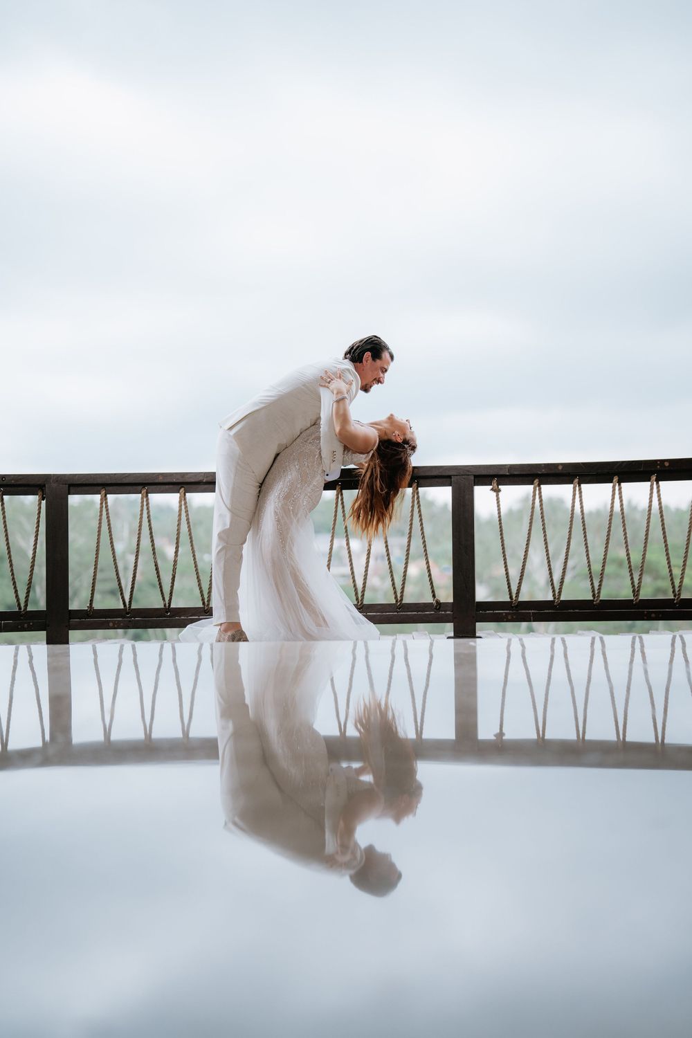 Artistic wedding dance sequence with reflections on white floor against cloudy sky.