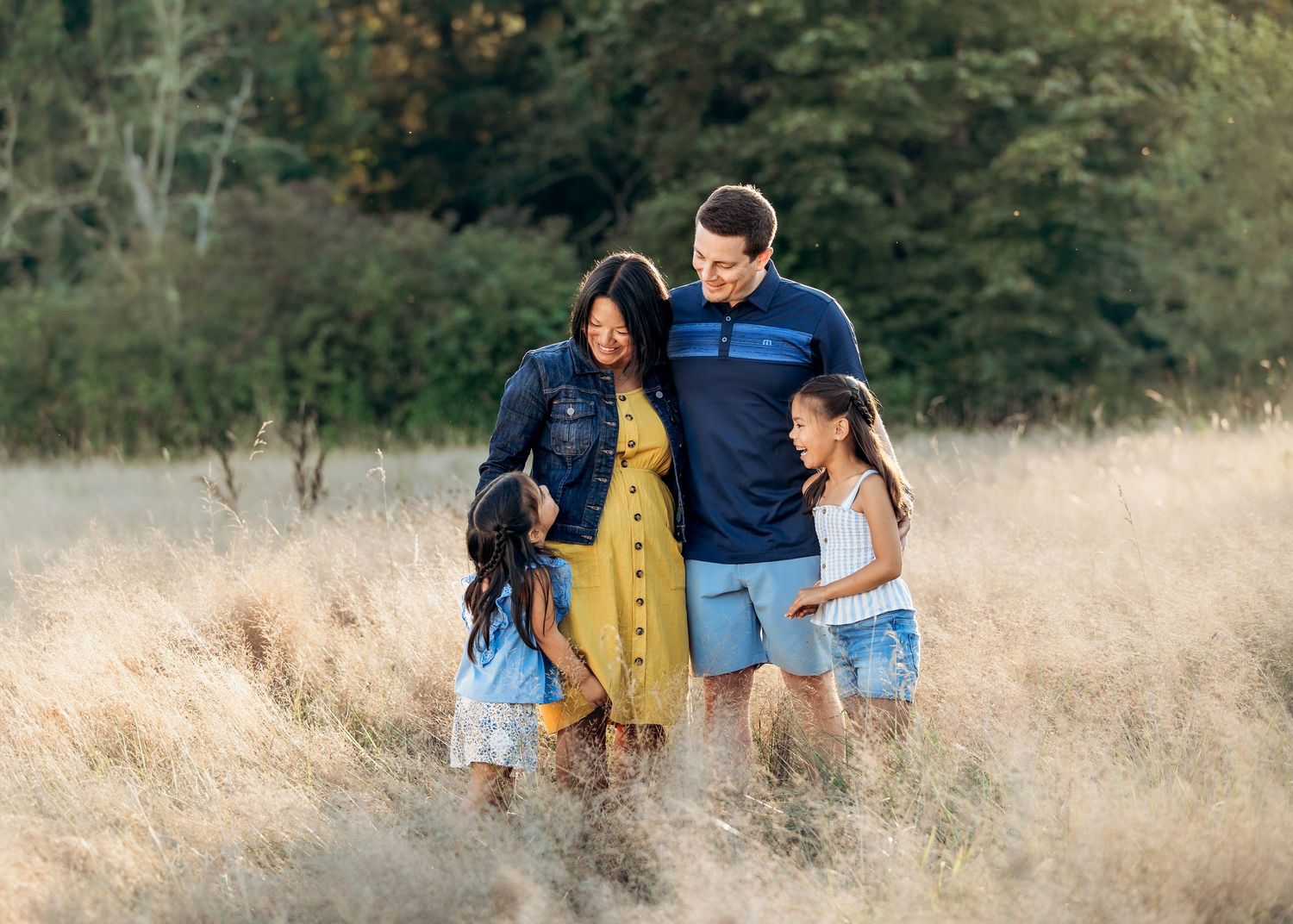 Family walking through golden grass field during sunset with mountains in distance.