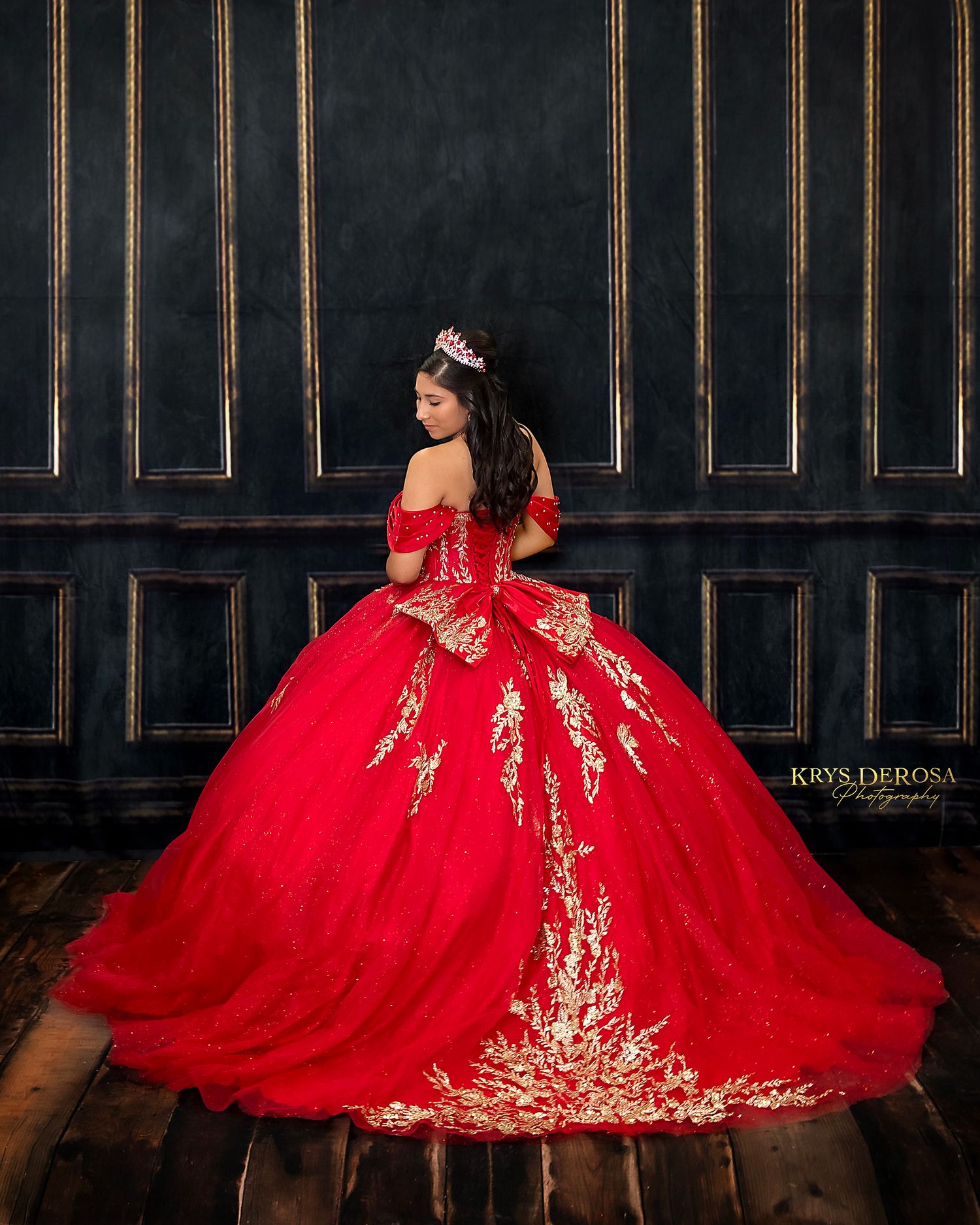 Stunning red and gold quinceañera ball gown with off-shoulder design and sparkly crown in dark elegant setting.