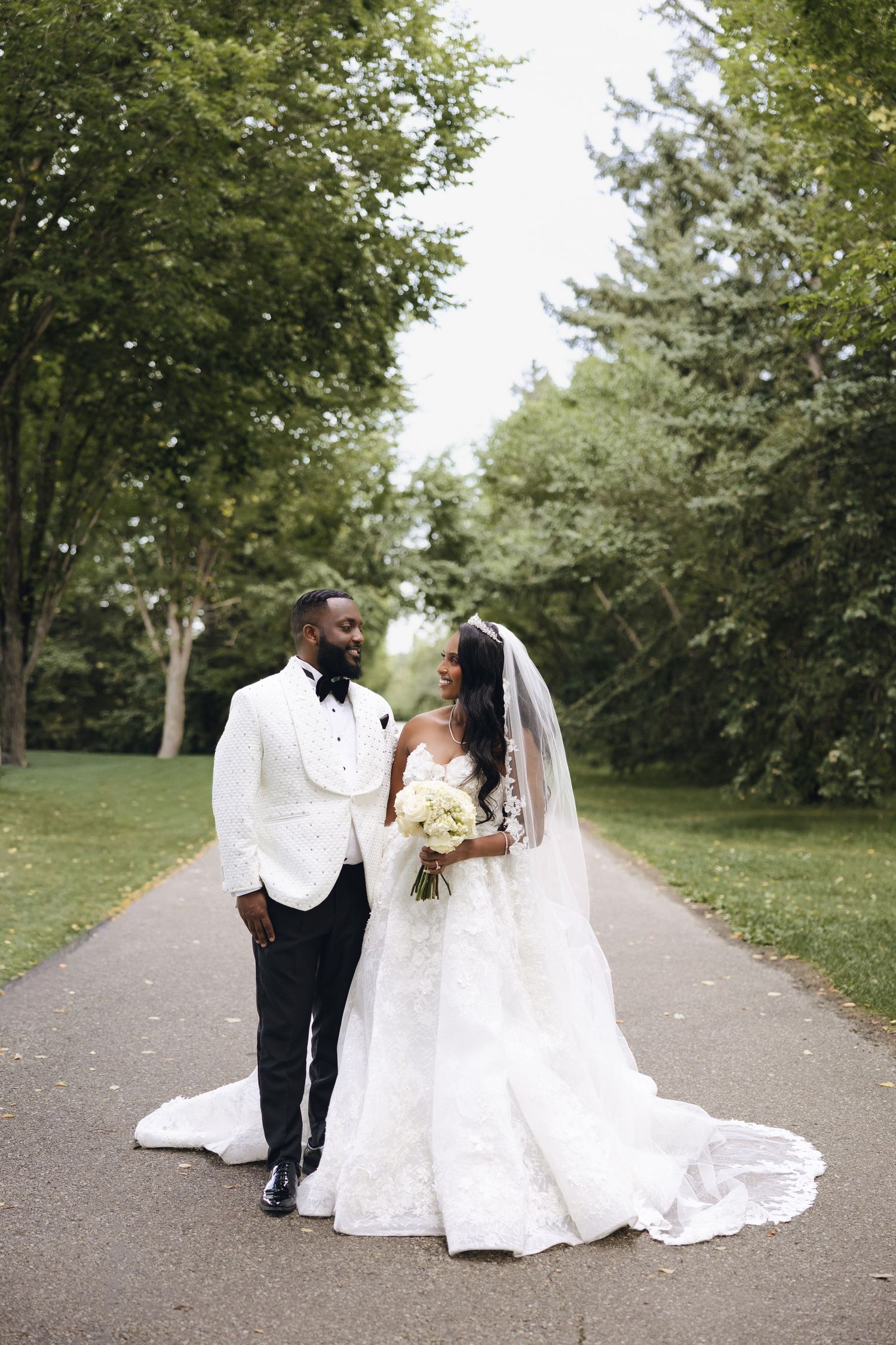 Happy newlyweds in elegant wedding attire run joyfully across a grassy lawn on their special day.
