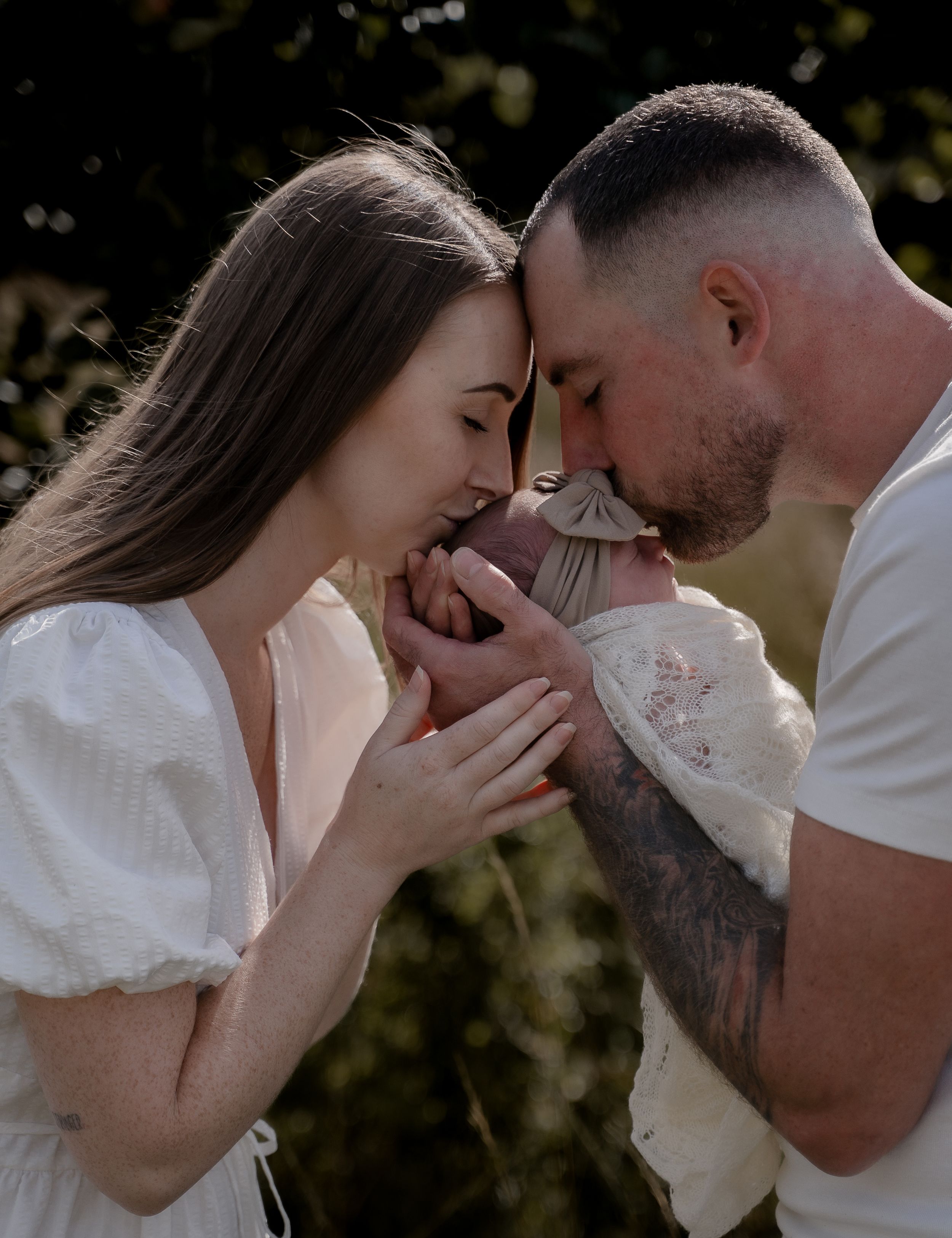 Mother and father kissing their newborn baby’s head in a heartfelt outdoor family lifestyle photography session in Derbyshire.