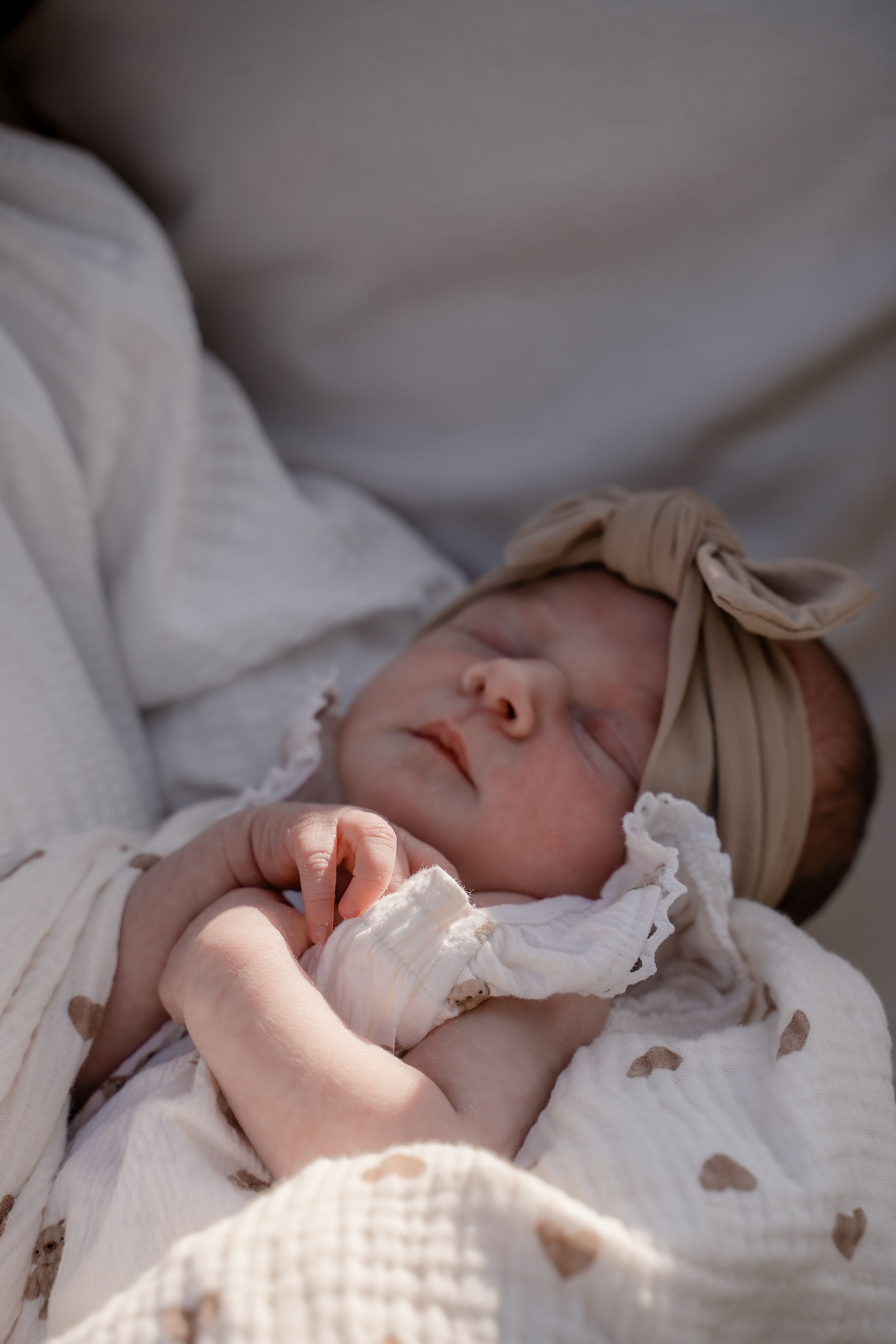 A sleeping baby in white clothing rests peacefully on soft bedding as sunlight streams across their face.