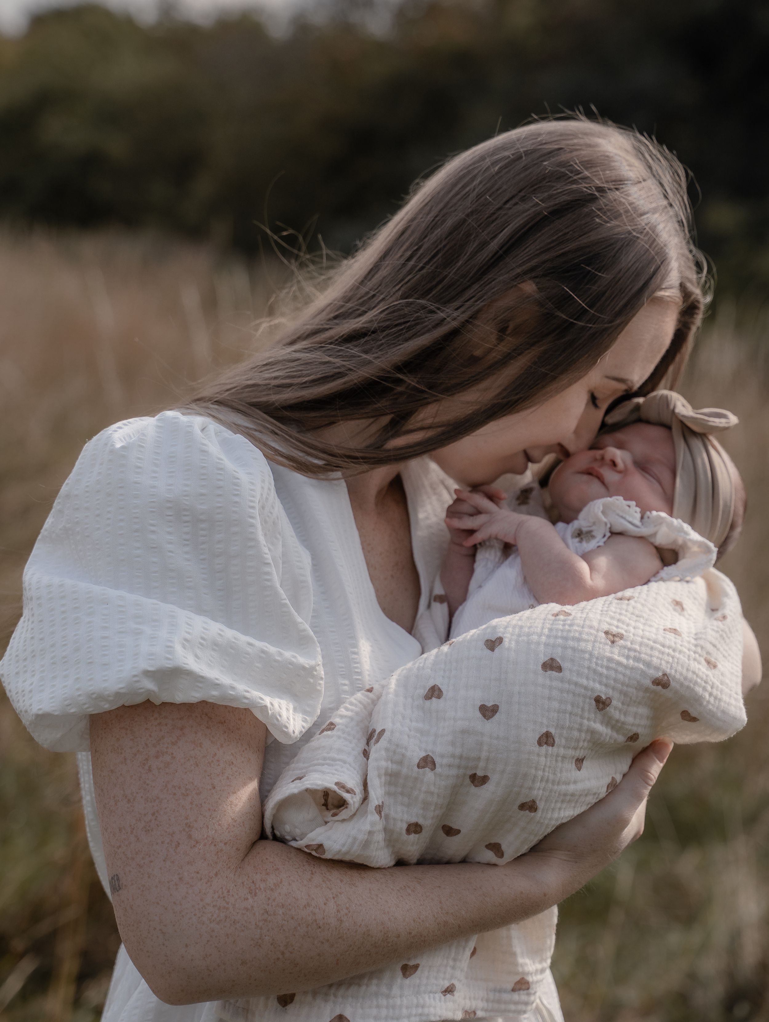Mother gently nuzzling her newborn baby, wrapped in a heart-patterned blanket, during an outdoor lifestyle session in Derbyshire.