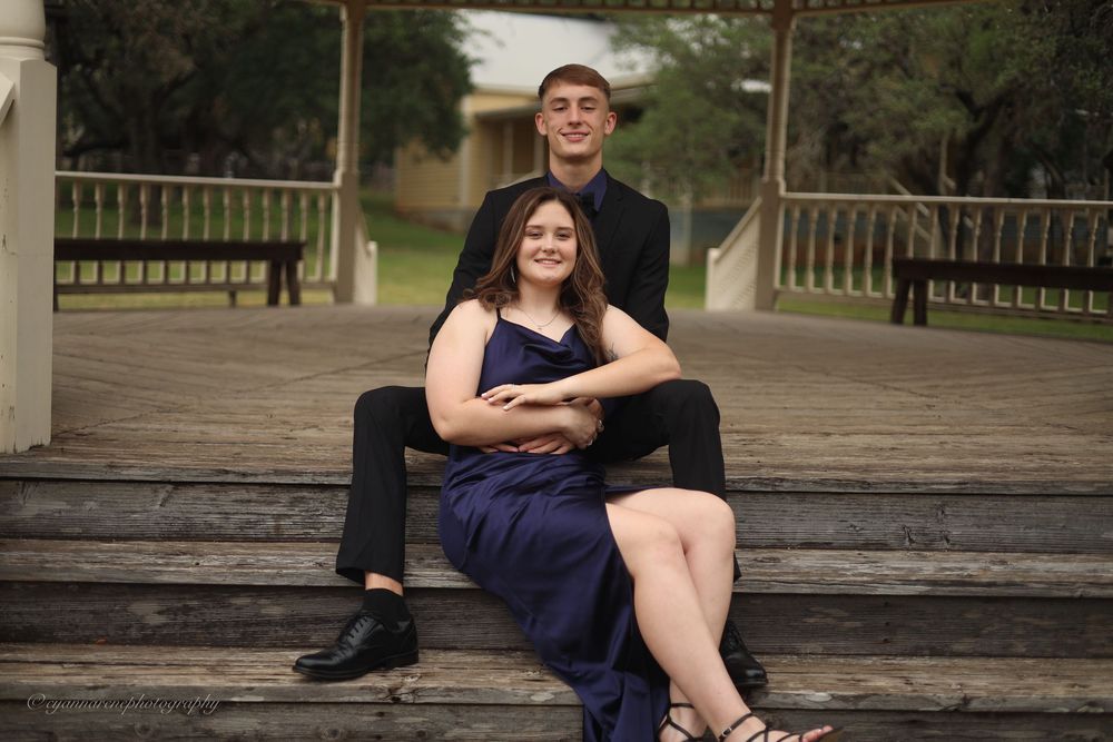 A person in a navy dress sits on weathered wooden steps during an outdoor photo session.