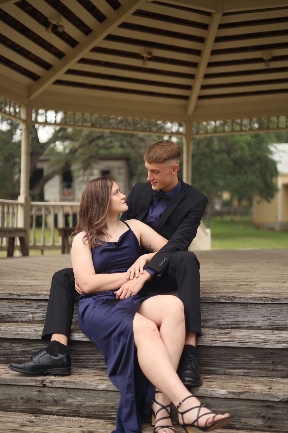 A couple shares an intimate moment together on a wooden bench under a gazebo.