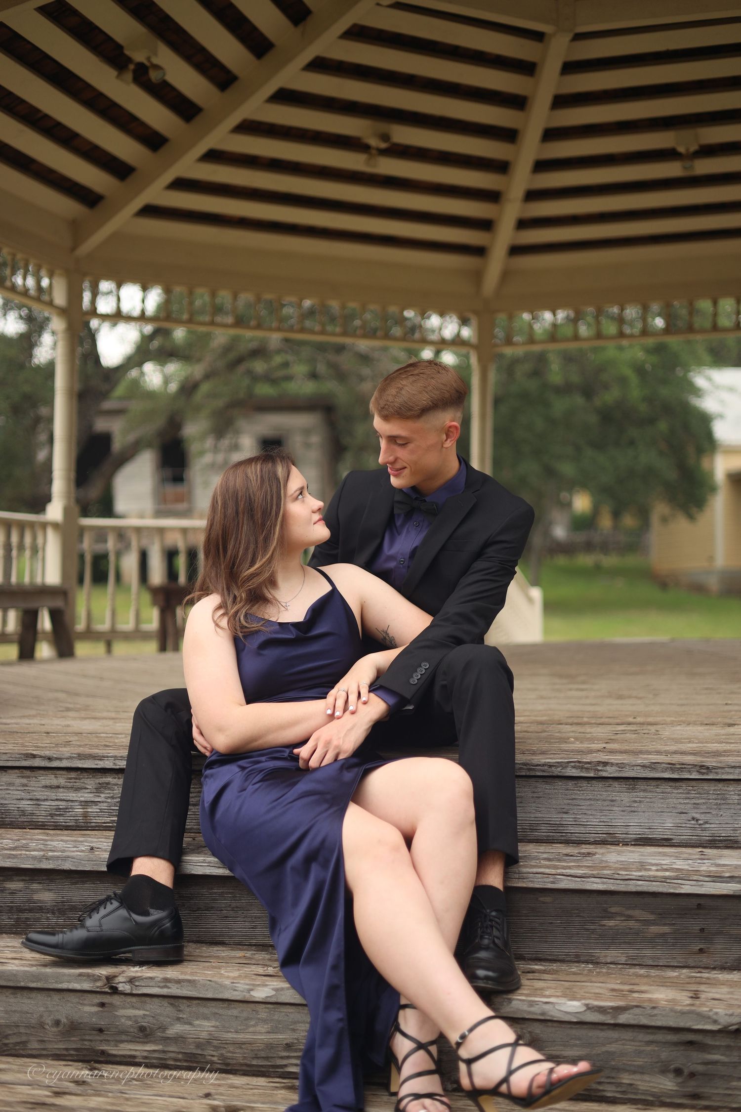 A couple shares an intimate moment together on a wooden bench under a gazebo.
