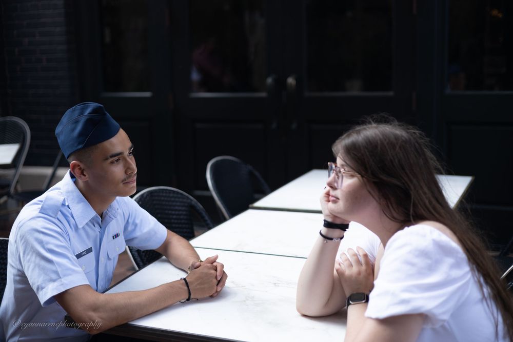 Two people having a conversation while seated at an outdoor table on a patio.