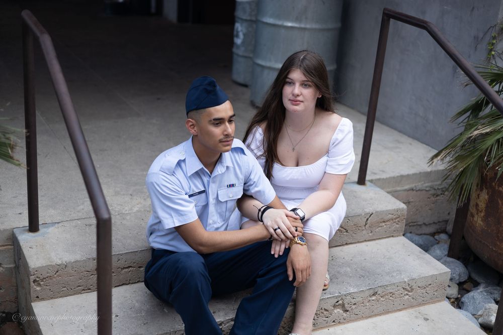 A couple sits close together on concrete steps outside a building, smiling and enjoying each other's company.