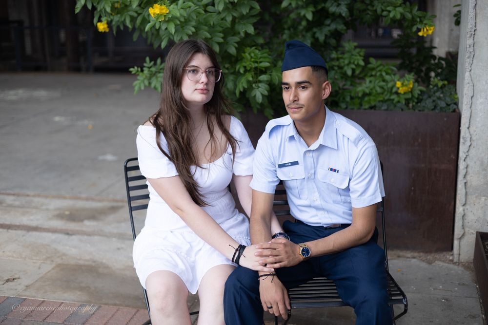 A couple in white and blue outfits pose together for engagement-style photos in an urban setting.