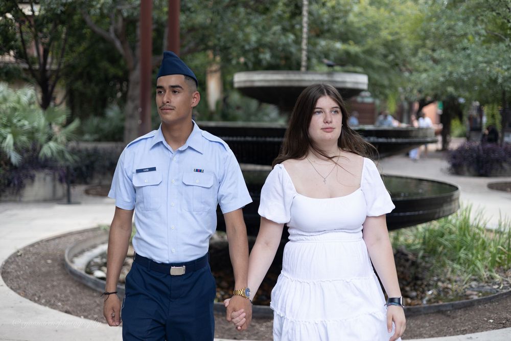 A couple walks through a garden pathway holding hands while wearing casual summer attire in the outdoors.