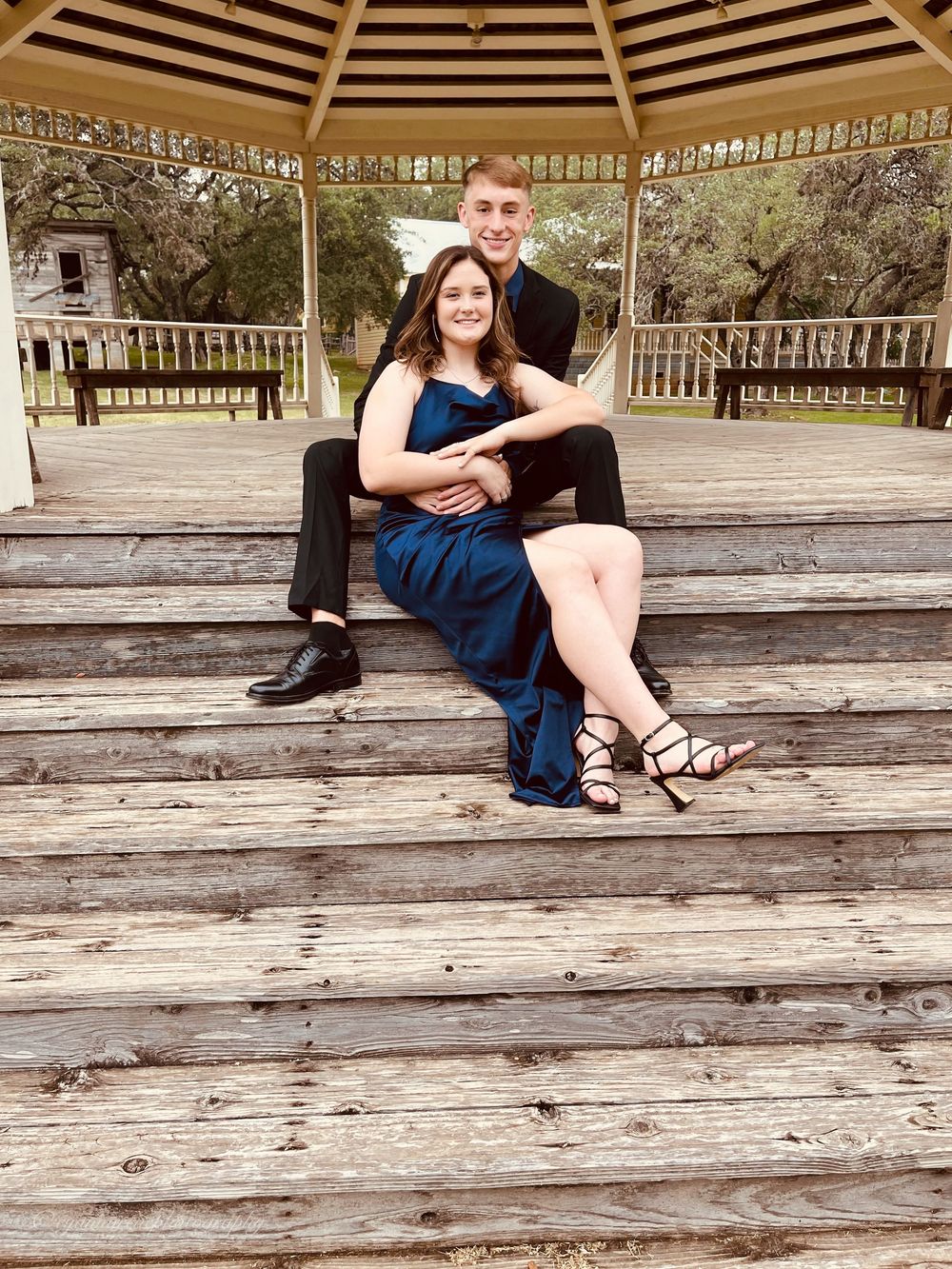 A couple sits together on a wooden gazebo deck on a sunny afternoon.