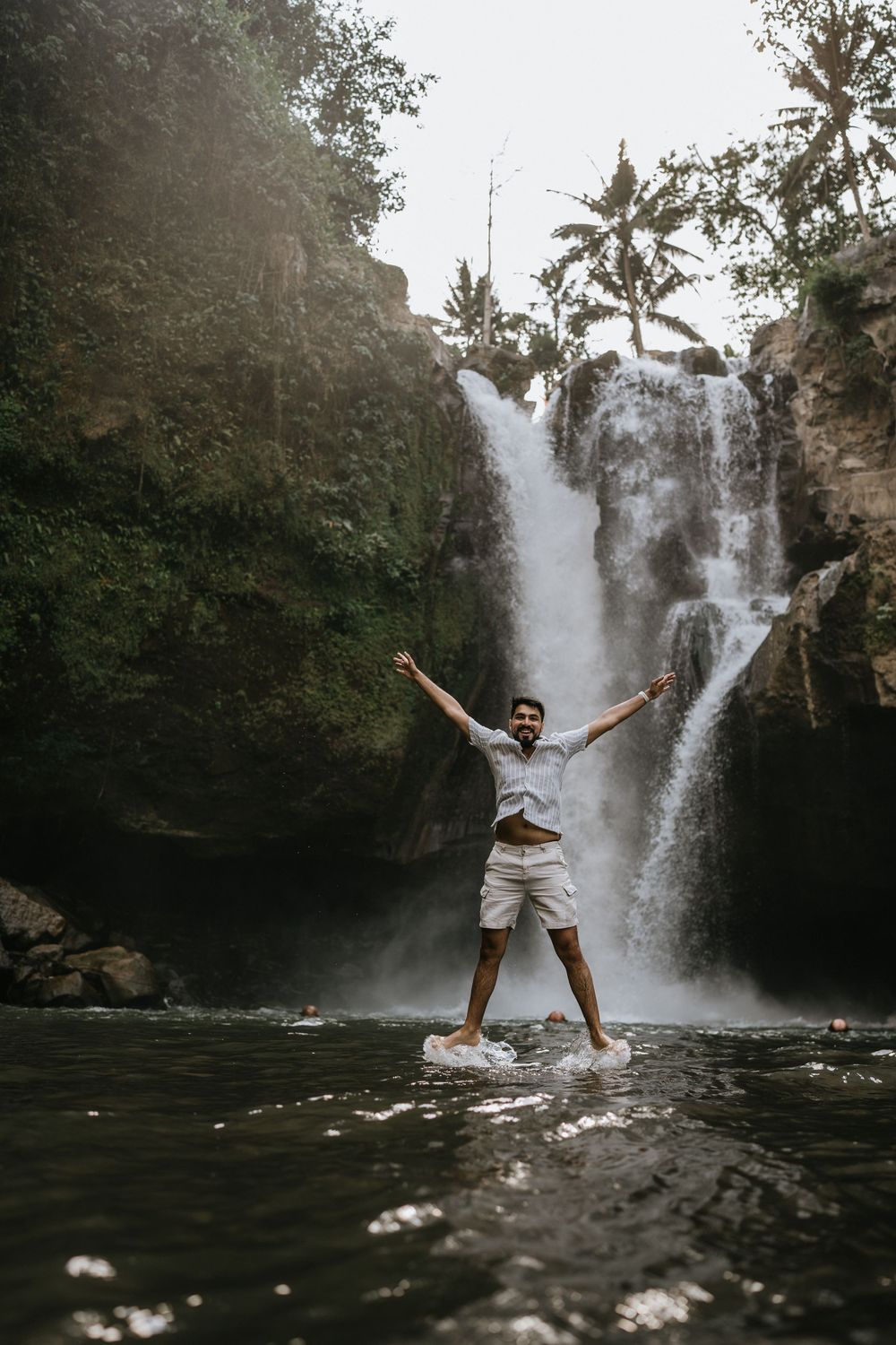 Person striking playful pose in front of majestic double waterfall.
