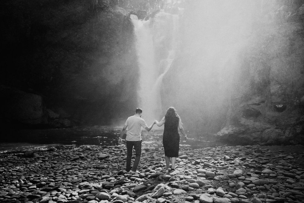 Silhouettes of people walking near misty waterfall at dusk.