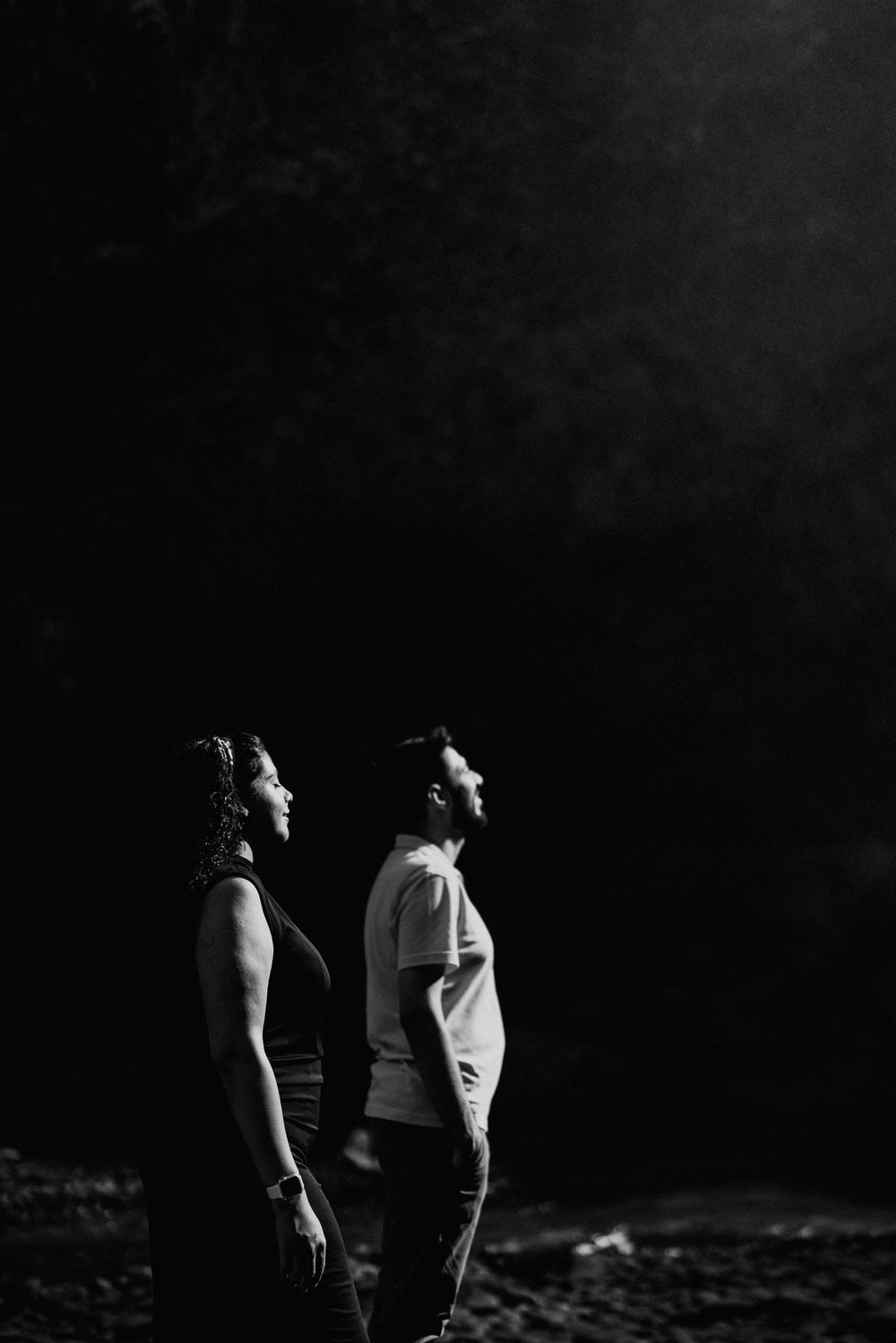 Dramatic black and white portrait of two people standing against a dark background.